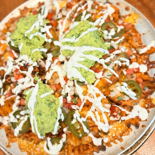 Loaded nachos topped with guacamole, white crema, diced tomatoes, cheese, and sliced jalapeños on a plate.