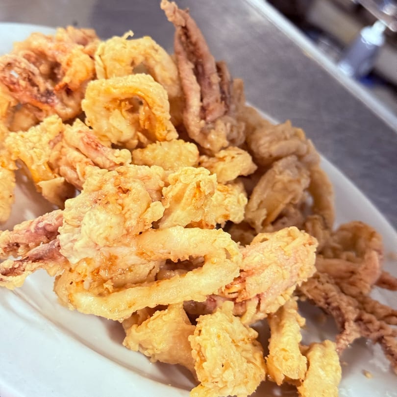 A close-up of a white plate piled high with golden-brown fried calamari rings and tentacles.