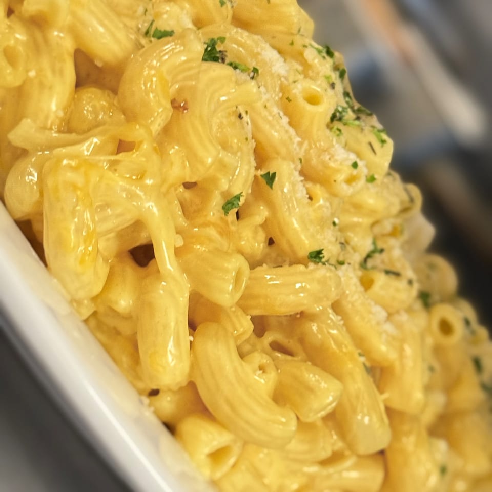 Close-up of creamy macaroni and cheese topped with parsley and grated cheese in a white bowl.