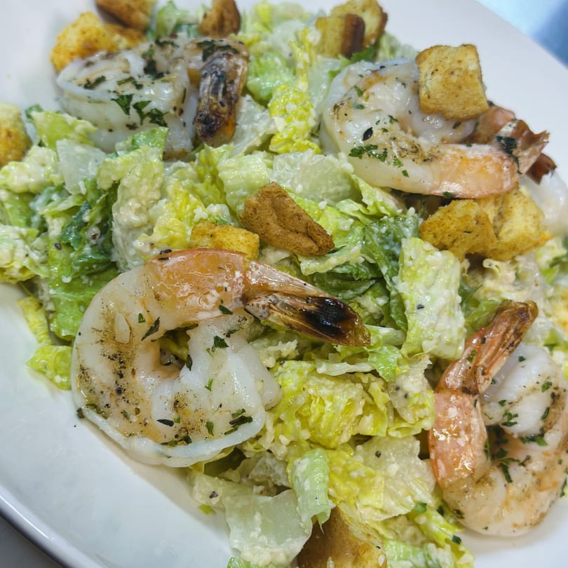 Caesar salad with grilled shrimp and croutons on a white plate.