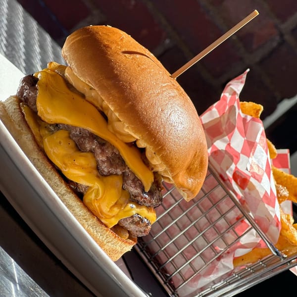 A double cheeseburger with melted cheese and a side of fries in a metal basket.