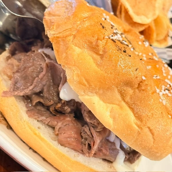 Close-up of a sesame-seeded sandwich roll filled with sliced roast beef and served with golden potato chips.