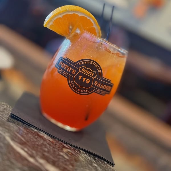 Pete's Saloon & Restaurant cocktail, orange drink with an orange slice and black straws.
