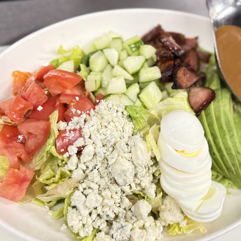 A vibrant Cobb salad with lettuce, tomatoes, cucumbers, blue cheese, bacon, avocado, and sliced hard-boiled eggs.
