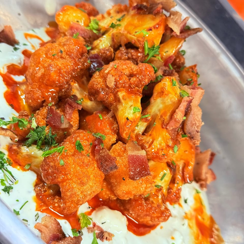 Pete's Saloon & Restaurant's buffalo cauliflower with bacon, ranch, and parsley in a white dish.