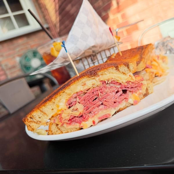 A close-up of a Pete's Saloon & Restaurant Reuben sandwich with fries in the background.