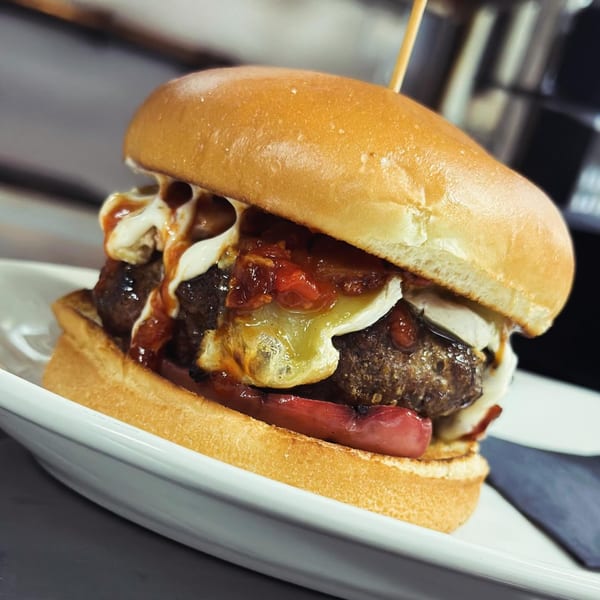 Close-up of a Pete's Saloon & Restaurant burger with melted cheese, sauce, and red peppers.