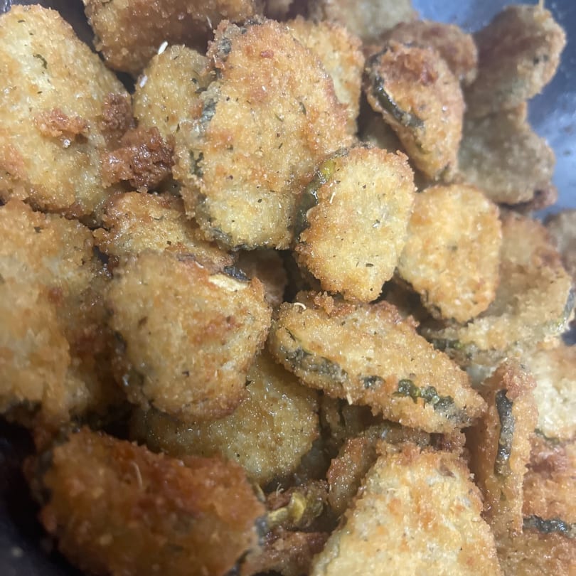 Close-up of golden-brown fried zucchini slices, coated in crispy breading with visible herbs.