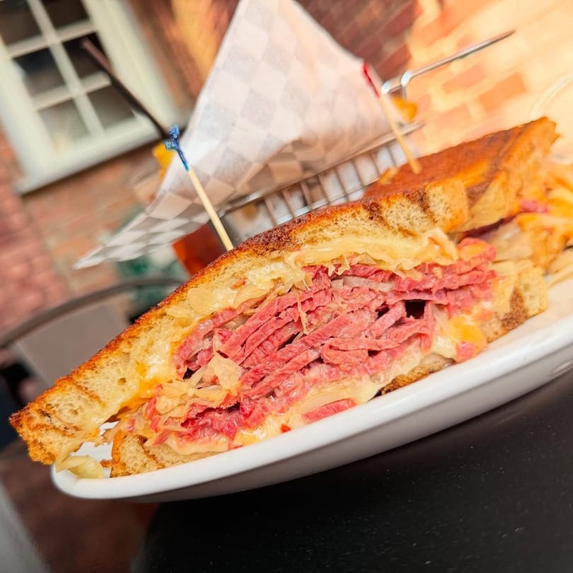 Close-up of a reuben sandwich with corned beef, sauerkraut, and melted cheese on toasted bread.