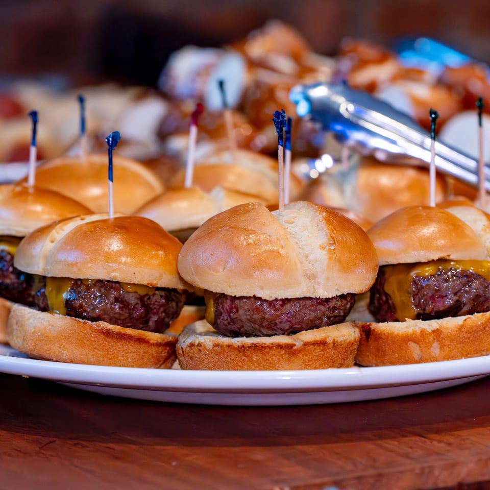 A white platter filled with mini cheeseburger sliders, each with a blue toothpick, at Pete's Saloon.