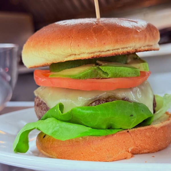 A Pete's Saloon & Restaurant burger with melted cheese, tomato, avocado, and lettuce on a bun.